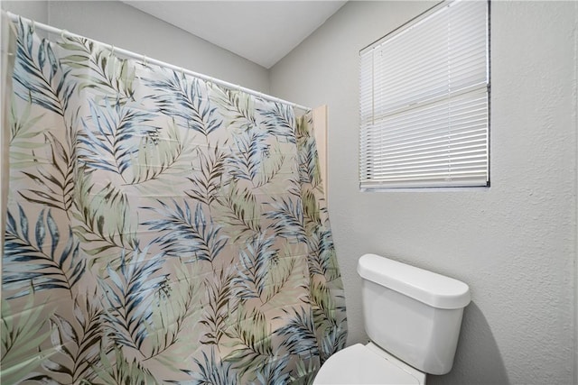 full bath with toilet, a shower with curtain, and a textured wall