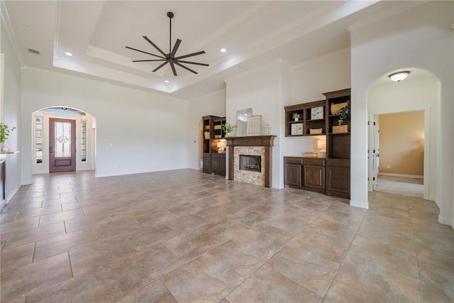 unfurnished living room featuring a high ceiling, a raised ceiling, ceiling fan, ornamental molding, and a fireplace