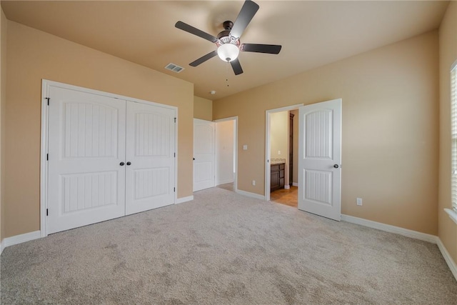 unfurnished bedroom featuring ceiling fan, ensuite bathroom, light carpet, and a closet