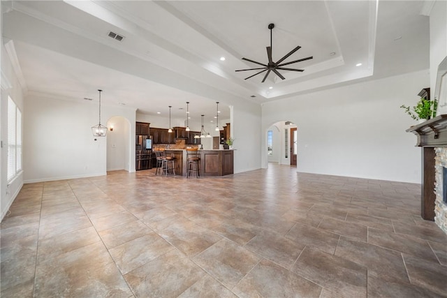 unfurnished living room with ceiling fan, a raised ceiling, a fireplace, and crown molding