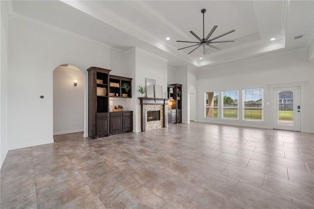 unfurnished living room with ceiling fan, crown molding, a towering ceiling, a tray ceiling, and a fireplace