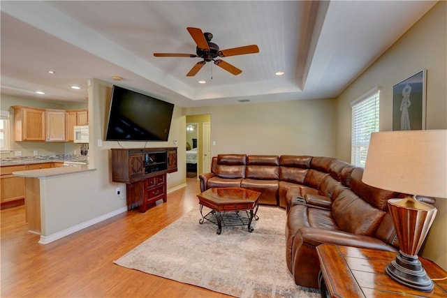 living room with light hardwood / wood-style floors, a raised ceiling, and ceiling fan