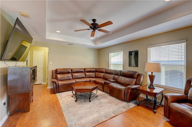 living room featuring ceiling fan, light hardwood / wood-style flooring, and a tray ceiling