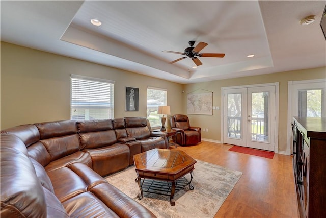 living room with light hardwood / wood-style floors, a raised ceiling, a wealth of natural light, and french doors