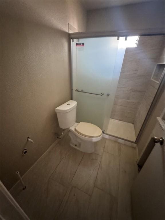 bathroom featuring a shower with shower door and toilet