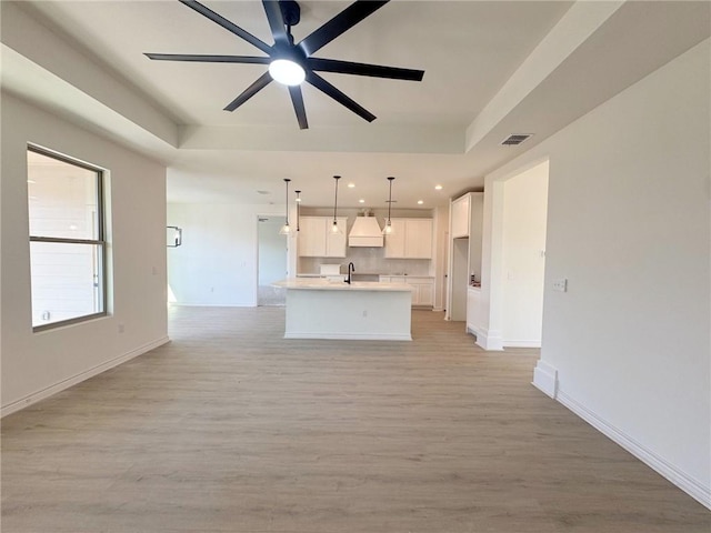 kitchen with sink, white cabinets, hanging light fixtures, a kitchen island with sink, and a raised ceiling