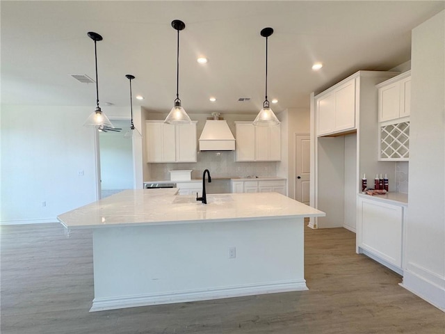 kitchen featuring hanging light fixtures, a center island with sink, white cabinets, and decorative backsplash