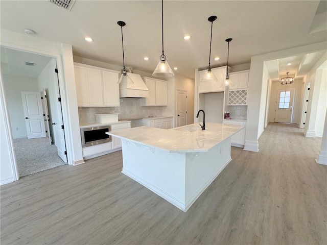 kitchen with sink, premium range hood, white cabinetry, a spacious island, and stainless steel microwave