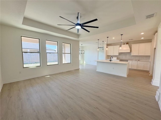 unfurnished living room featuring a raised ceiling, sink, and light hardwood / wood-style flooring