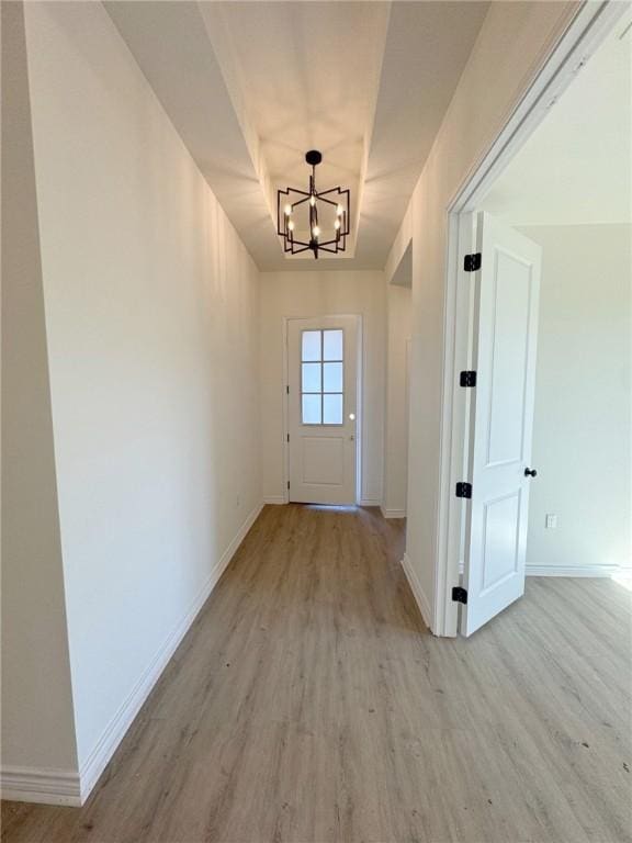 doorway to outside with an inviting chandelier, a tray ceiling, and light wood-type flooring