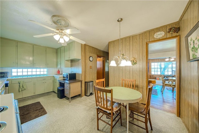 dining room featuring wooden walls and ceiling fan with notable chandelier