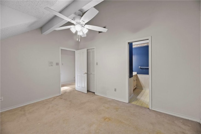 unfurnished bedroom with ensuite bathroom, lofted ceiling with beams, light carpet, a textured ceiling, and ceiling fan