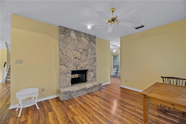 living room featuring ceiling fan, hardwood / wood-style floors, a textured ceiling, and a fireplace