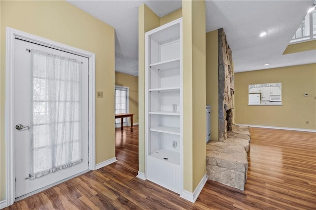 hallway with built in shelves, dark hardwood / wood-style floors, and a textured ceiling