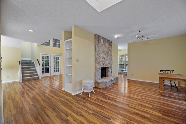 living room with french doors, a stone fireplace, dark hardwood / wood-style flooring, and a textured ceiling