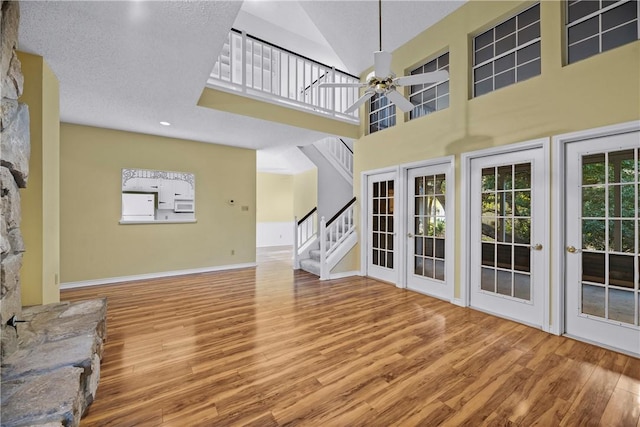 unfurnished living room featuring a towering ceiling, hardwood / wood-style floors, ceiling fan, and french doors