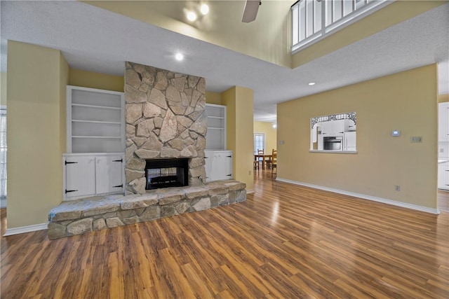 unfurnished living room with a towering ceiling, a fireplace, hardwood / wood-style flooring, ceiling fan, and built in shelves