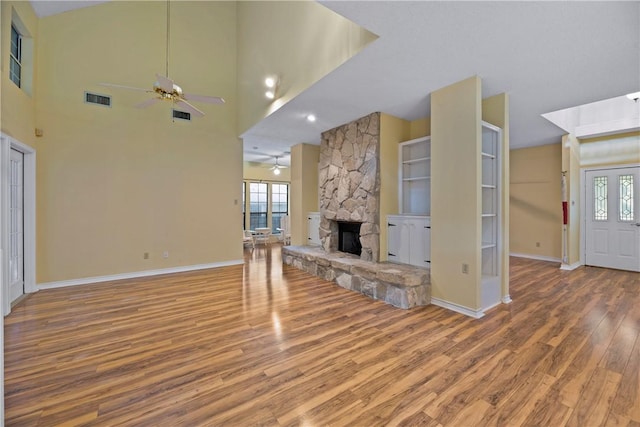 unfurnished living room featuring a stone fireplace, wood-type flooring, ceiling fan, and a high ceiling