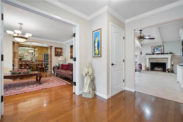 interior space featuring crown molding, baseboards, ornate columns, wood finished floors, and a notable chandelier