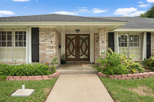 view of exterior entry with roof with shingles and brick siding