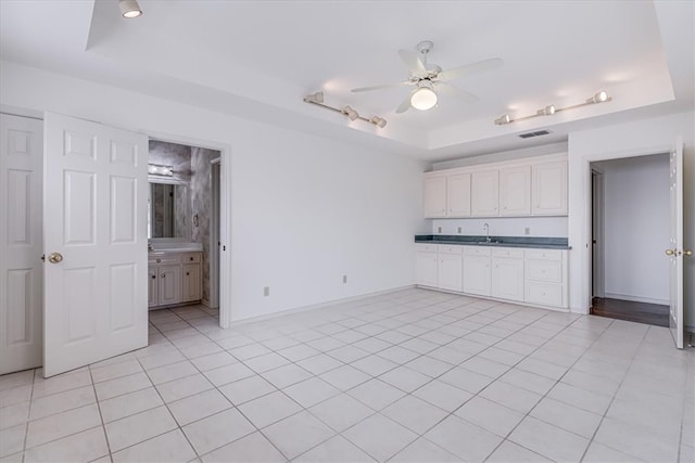 interior space featuring connected bathroom, light tile patterned floors, ceiling fan, and a raised ceiling