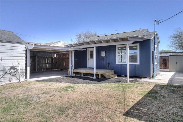 view of front facade with a carport, a shed, a front yard, roof with shingles, and an outbuilding