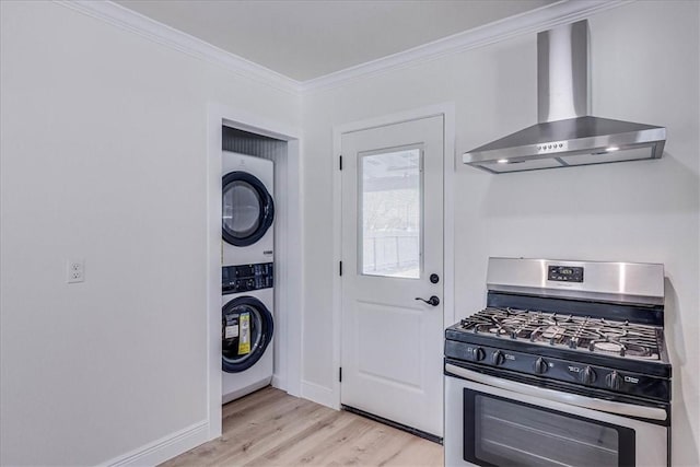 kitchen with stainless steel gas range oven, stacked washer / dryer, wall chimney range hood, light wood-type flooring, and ornamental molding