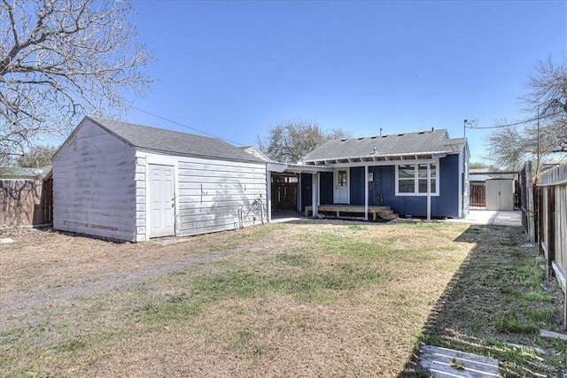 rear view of property featuring an outbuilding, a yard, a fenced backyard, a shingled roof, and a storage shed