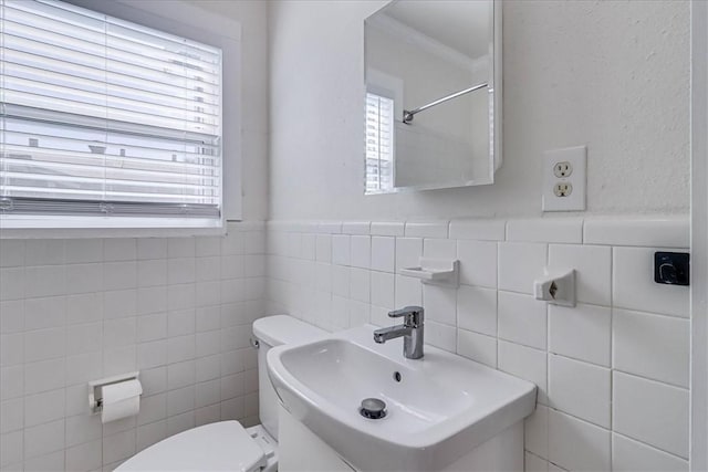 bathroom featuring a wainscoted wall, toilet, tile walls, and a sink