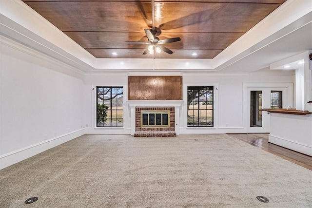 unfurnished living room with ceiling fan, a fireplace, a tray ceiling, and carpet flooring