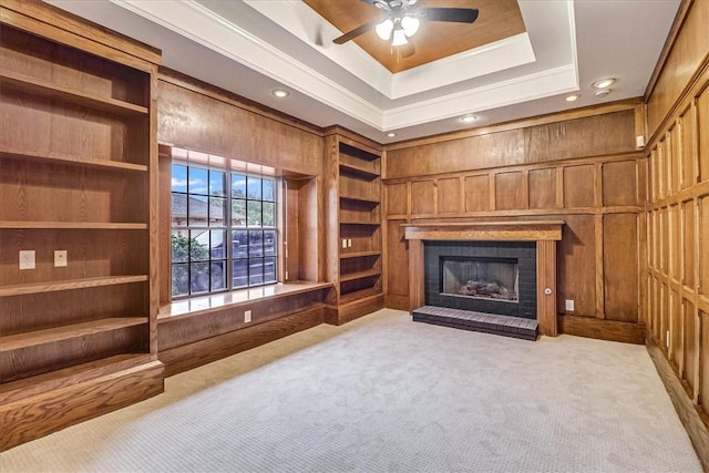 living room featuring wooden walls, a tray ceiling, a brick fireplace, light carpet, and built in shelves