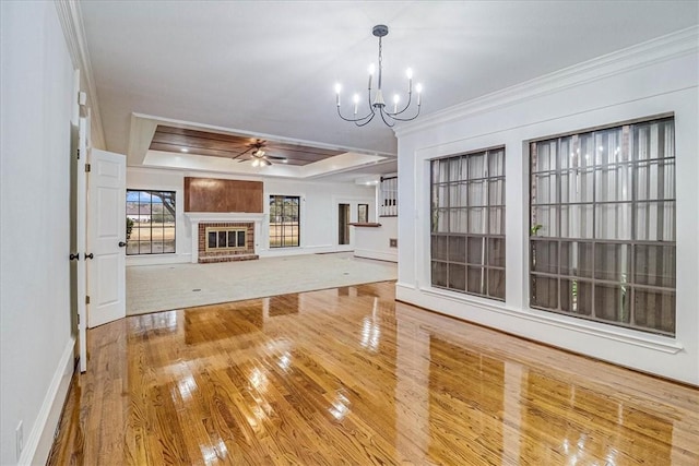 unfurnished living room featuring crown molding, a raised ceiling, hardwood / wood-style floors, a fireplace, and ceiling fan with notable chandelier