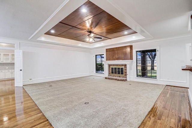 unfurnished living room featuring ceiling fan, ornamental molding, a raised ceiling, and a brick fireplace