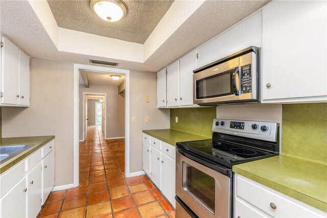 41 Townhouse, Corpus Christi, TX 78412 - kitchen featuring appliances with stainless steel finishes, a tray ceiling, white cabinetry, baseboards, and light tile patterned floors