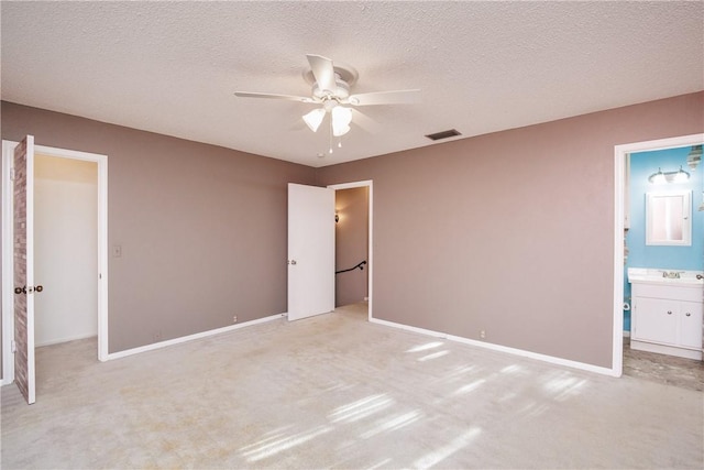 unfurnished bedroom featuring light carpet, a textured ceiling, ensuite bath, and ceiling fan