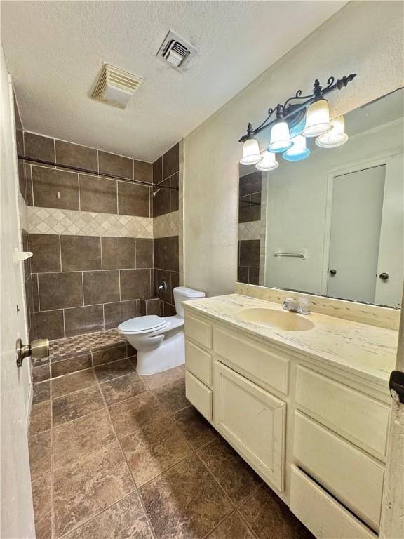 bathroom with a tile shower, vanity, a textured ceiling, and toilet