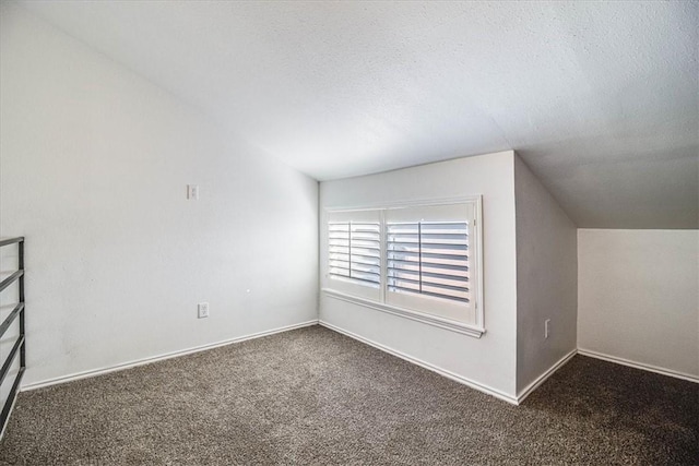 additional living space with dark colored carpet, vaulted ceiling, and a textured ceiling