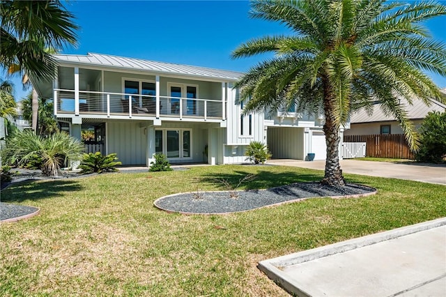 exterior space featuring a balcony, fence, a standing seam roof, a yard, and concrete driveway