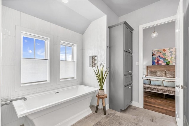 ensuite bathroom with a freestanding bath, vaulted ceiling, tile patterned floors, and ensuite bathroom