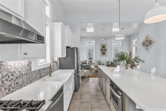 kitchen featuring tasteful backsplash, appliances with stainless steel finishes, white cabinetry, a sink, and wall chimney exhaust hood