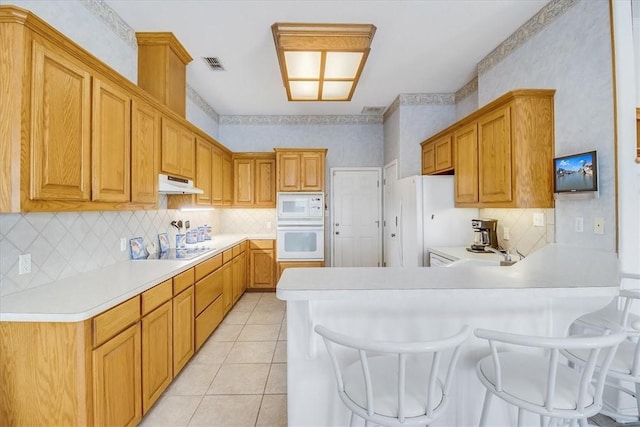 637 Pompano Dr, Aransas Pass, TX 78336 - kitchen featuring white appliances, under cabinet range hood, a peninsula, and backsplash