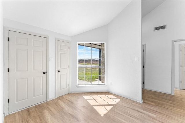 unfurnished bedroom featuring visible vents, baseboards, high vaulted ceiling, and light wood-style flooring