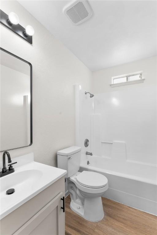 full bathroom with visible vents, toilet, wood finished floors, washtub / shower combination, and vanity