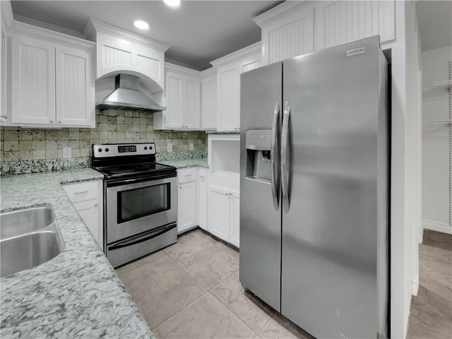 kitchen with white cabinets, wall chimney range hood, tasteful backsplash, light stone counters, and stainless steel appliances