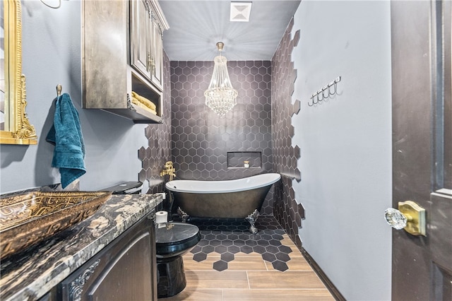 bathroom featuring an inviting chandelier, a tub to relax in, toilet, vanity, and hardwood / wood-style flooring