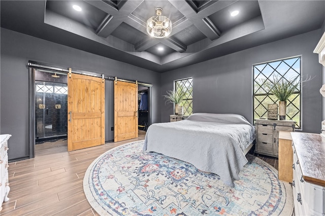 bedroom with beam ceiling, a barn door, light hardwood / wood-style flooring, and coffered ceiling