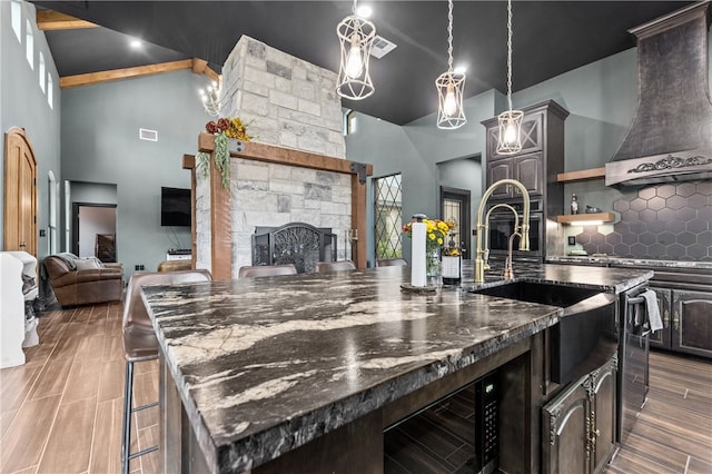 kitchen with high vaulted ceiling, a stone fireplace, wall chimney exhaust hood, a large island, and a kitchen bar