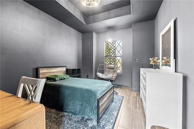 bedroom featuring light wood-type flooring, an inviting chandelier, and a raised ceiling