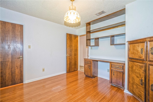 kitchen with a textured ceiling, light wood-type flooring, built in desk, and decorative light fixtures