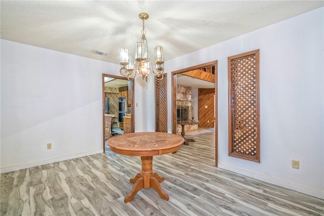 unfurnished dining area featuring a fireplace, hardwood / wood-style floors, a notable chandelier, and a textured ceiling